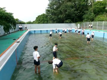 プールで市と生徒たちが水を汲んだり泥を取り除いたりしながら清掃作業をしている