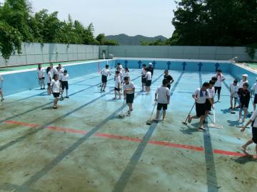 屋外のプールで生徒達がブラシやほうきで掃除している様子