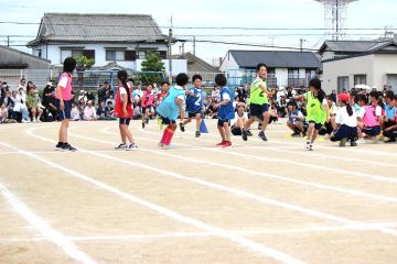 校庭のトラック上で地区別対抗リレーでバトンパスを行う児童たちの様子