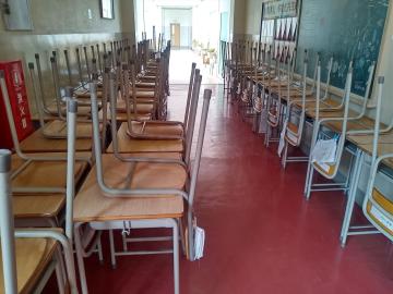 教室内で椅子が机の上に裏返して列になって置かれ廊下に続く空の教室の風景