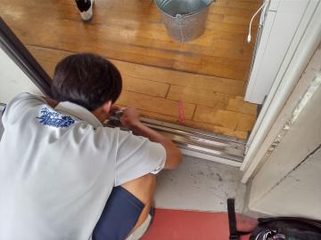 体操服の生徒が屋内のドア下のレールを床にしゃがんで手で調整している