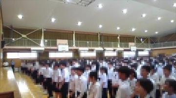 体育館に整列して制服を着た多数の生徒が集まり講壇側を向いている光景