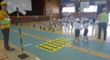 体育館で指導者に見守られながら子どもたちが踏切を渡る練習をしている様子