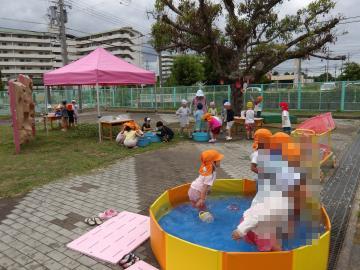 屋外で、子供たちが小さなビニールプールや水鉄砲などで遊んでいる風景