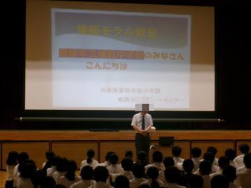 体育館のステージの前に講師の先生が立ち、自己紹介をしています。