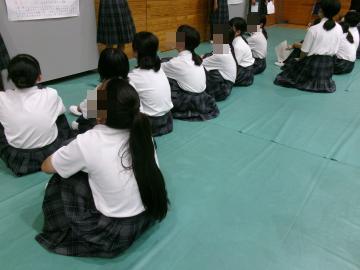 生徒が横一列に並んで床に座り、前方のポスターを見ています。