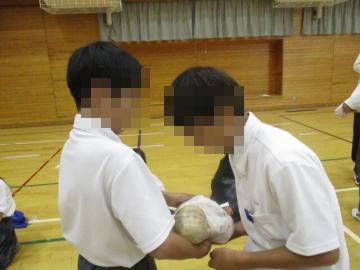 体育館で2人の生徒が乳児の人形を抱えて向き合っている。