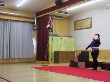 遊戯室の舞台で高い竹馬に乗る猿とスタッフの女性