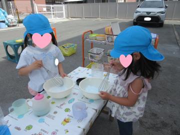 庭でテーブルを出しその上で泡だて器とボウルを使って泡クリームを作っている写真