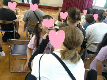 遊戯室で椅子に座った親が立っている子どもの歯を磨いている