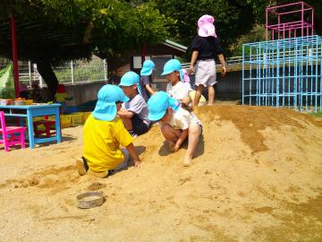 真砂土の山に座り込んで、土を触って感触を楽しんでいる5歳児