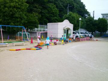 園庭を横切るほど長く並べられた雨どいの周りで子供たちが銘々に水を流している