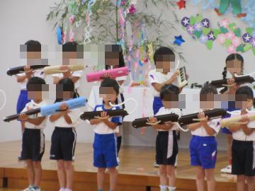 七夕の飾りが施された壁の前の舞台に並んだ子どもたちが色とりどりの鍵盤ハーモニカを持って並んで演奏している