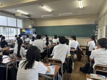 教室内で、英語の授業中にプレゼンテーションする交換留学生を見守る生徒たちの様子