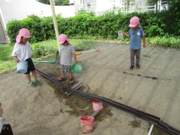 砂場で樋に水を流して遊んでいる様子