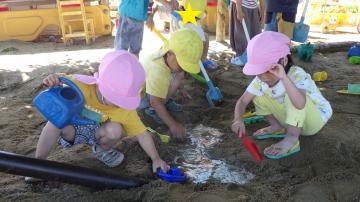 3、4歳児が砂場で穴を掘って水路をつくっている様子