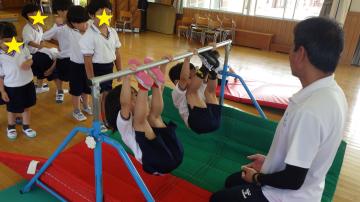 4歳児の運動遊びで、鉄棒のぶら下がりに挑戦している様子