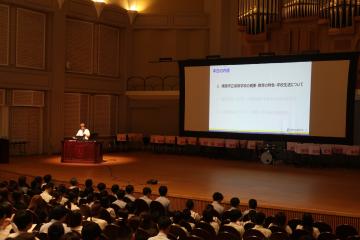 壇上でスクリーンに資料を写し、学校説明する教頭の様子