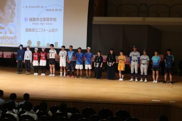 壇上で、運動部によるユニフォーム紹介が行われる様子。生徒たちが横一列に整列しています。