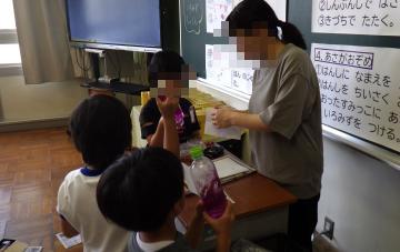 先生へ色水を見せている児童3人