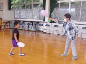 幼児が老人クラブの方と風船の打ち合いをする様子