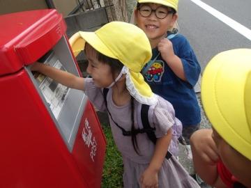 幼児が嬉しそうな表情でポストにハガキを投函する様子