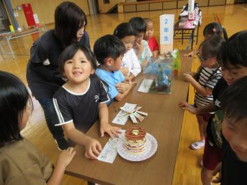 机の上に並べて飾ってある作品を見ている子供たちと、こちらに向かって笑顔を向ける子供