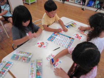 平仮名表を机の真ん中に置き、ハガキに絵や文字をかく子供たち