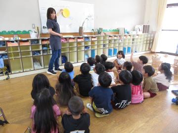 月を形に切った画用紙を使い、話をする教師と座って話を聞く子供たち