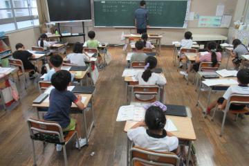 教室で児童が机に向かい教師が黒板に立って授業している様子
