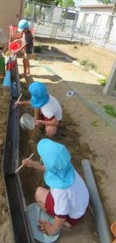 数人の子どもが屋外で並べた樋沿いに座り箸をもってそうめんが流れてくるのを待つ様子