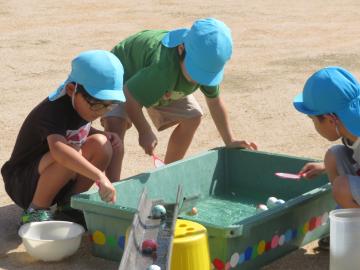 子どもたちが屋外で大きな桶のスーパーボールすくいをしている様子