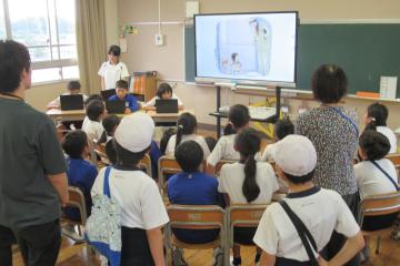 教室内で、給食委員会のメンバーのお話を映像を見ながら聴いている児童の様子