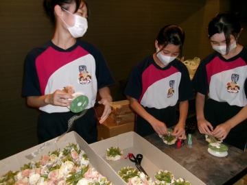 生徒3人がテーブルで小さな花束を手作業で作る様子