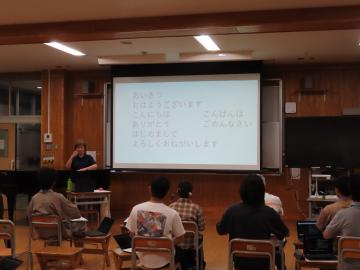 教室でスクリーンを使って説明する講師と複数の学生が列になって座っている様子