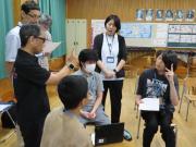 教室で数人の生徒と教員が円になって座り指文字を確認しあっている場面