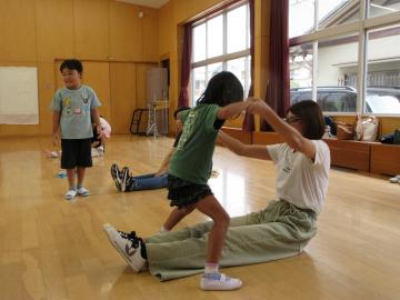 親が座って足を開閉し、子供は親の足を踏まないようにジャンプしている様子