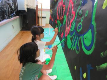 女の子二人が、絵具を使って黒い画用紙に宇宙の絵を描いている様子