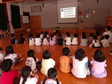 遊戯室に並んで座る子どもたちがスクリーンの月の映像を見ている