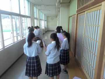 数名の生徒が学校の廊下で資料を手に立ち並んで練習している