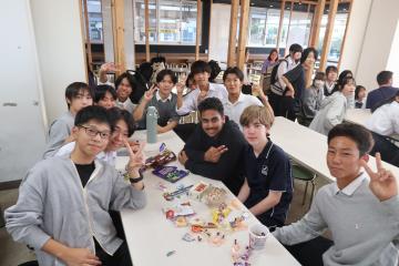 キャンパスの食堂でテーブルを囲んで座りお菓子を並べて笑顔でカメラを見る若者たちのグループ