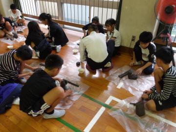 体育館の床に座ってビニールシートの上でシャチホコを作る児童たちの様子