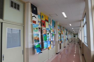 廊下の片側の壁に児童の絵画や作品がカラフルに貼られ窓から自然光が差し込む学校の長い廊下