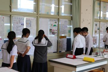教室の窓際に展示されたポスターや資料を制服の中高生が数人で見学している風景