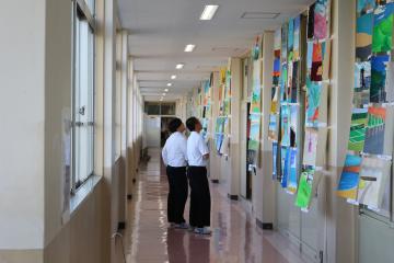 学校の廊下で展示された作品を並んで見ている制服の生徒二人の後ろ姿