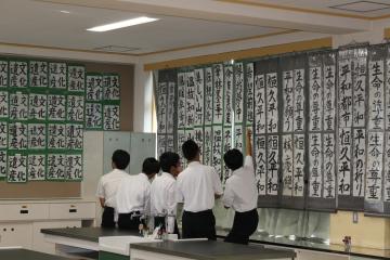 教室の壁に掛けられた書道作品を制服姿の生徒たちが並んで見ている