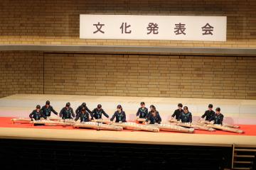 舞台で生徒たちが箏を並べて演奏している背景に文化発表会の横断幕が掲げられている