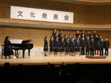 舞台上でピアノ伴奏に合わせて制服を着た児童と生徒が合唱している文化発表会の様子