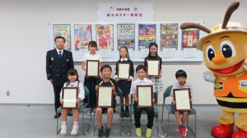 表彰状を掲げて記念撮影をする児童7人と消防局長