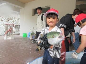 赤い帽子をかぶった子どもが大きな魚を抱きかかえている様子